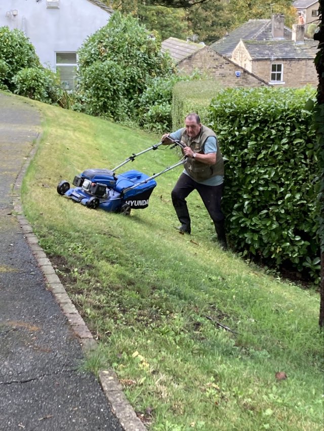 Volunteer mowing the lawn on a sloped area in the Memorial Gardens